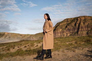 A stylish black leather trench coat worn by a model on a city street, showcasing a sleek, modern design with a belted waist