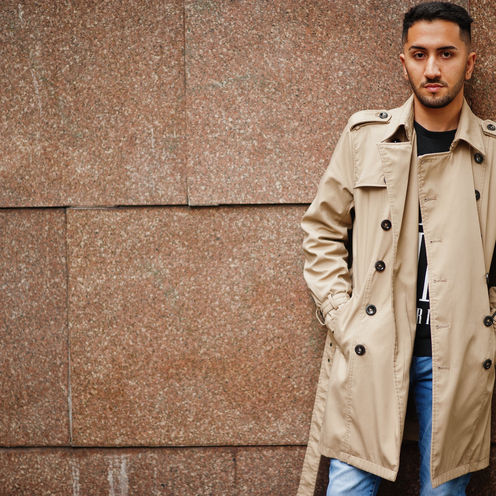 A brown leather trench coat styled with a cream sweater and jeans, photographed outdoors on a crisp autumn day.