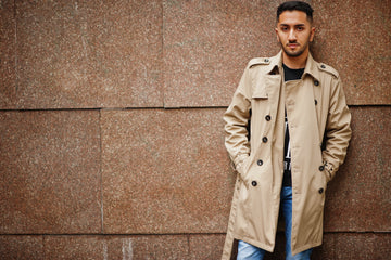 A brown leather trench coat styled with a cream sweater and jeans, photographed outdoors on a crisp autumn day.